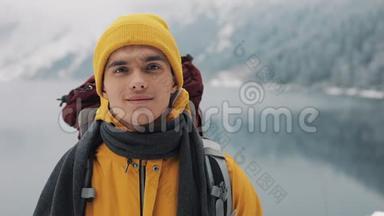 穿着冬装的年轻迷人男子的肖像。 穿着黄色冬装的徒步旅行者看着摄像机